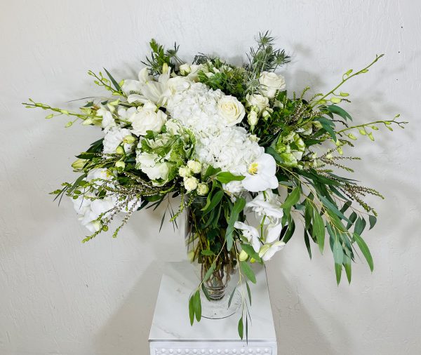 Regal Whites white kale, white roses, white phalaenopsis orchids, white dendrobium orchids, spray roses, thistle, and white asiatic lilies in a pedestal vase