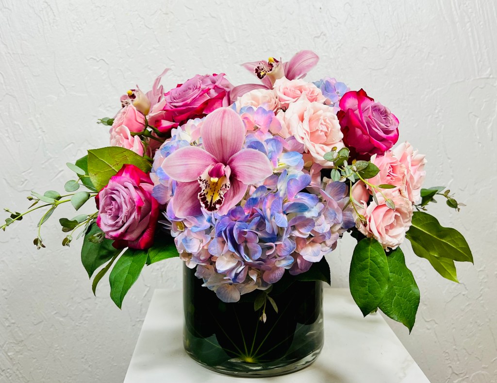 pink and blue hydrangeas, pinkle roses, pink spray roses, pink cymbidium orchids in a low cylinder designed by La Paloma Blanca Floral Designs in Scottsdale, AZ