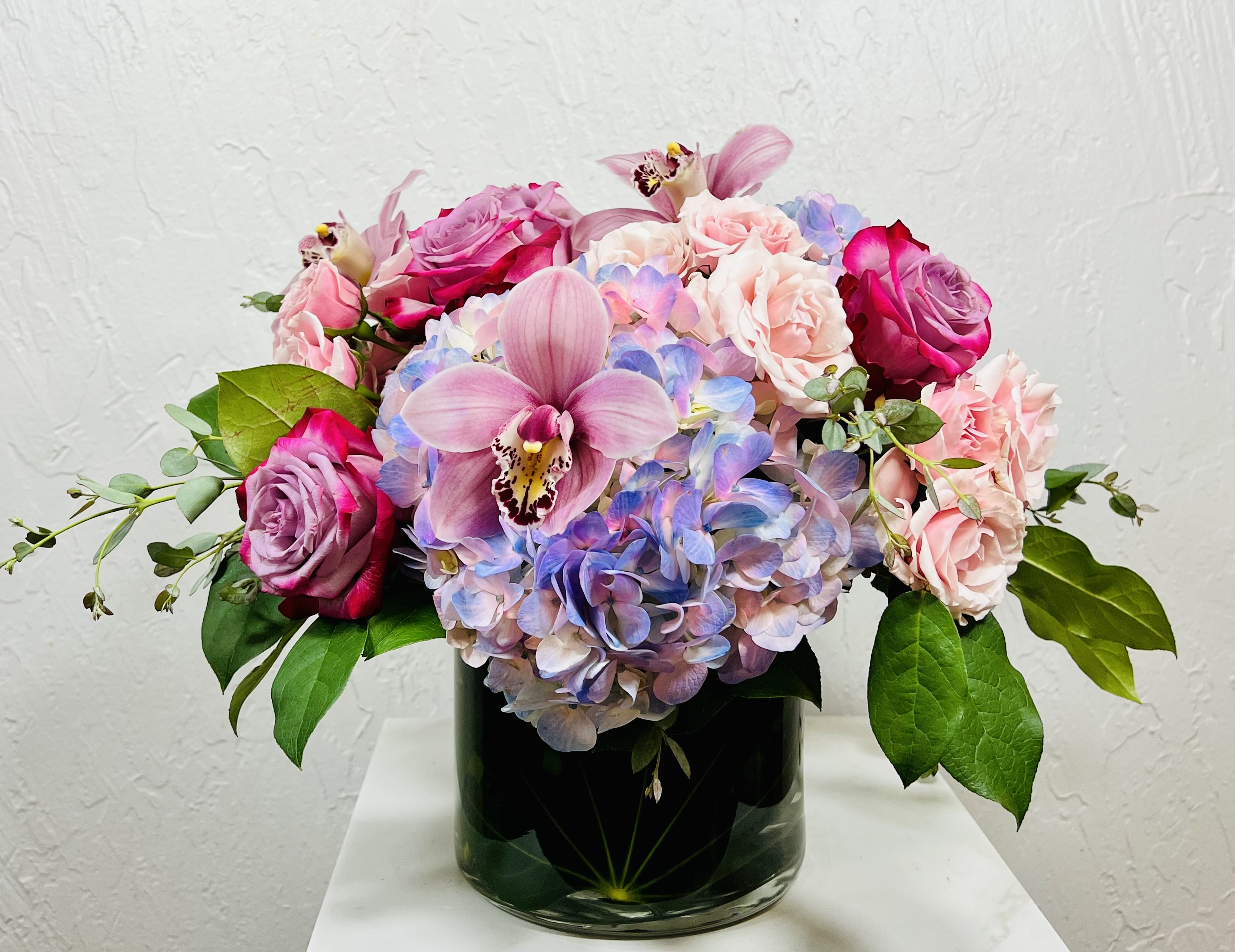 pink and blue hydrangeas, pinkle roses, pink spray roses, pink cymbidium orchids in a low cylinder designed by La Paloma Blanca Floral Designs in Scottsdale, AZ