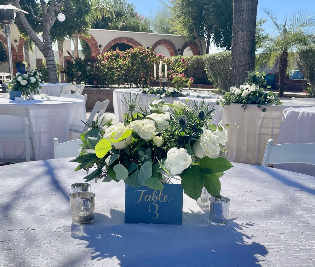 centerpiece with white roses, white anemone, thistle and greens with a table 3 sign in front