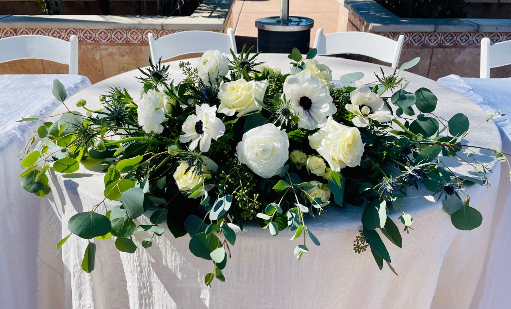 white roses, white ranunculus, white anemone, and thistle large and draped over a table