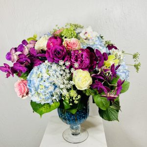 Pedestal Vase with blue crystal on the bottom, blue hydrangea, pink, purple, and white roses, cymbidium orchids, phalaenopsis orchids designed by La Paloma Blanca Floral Designs