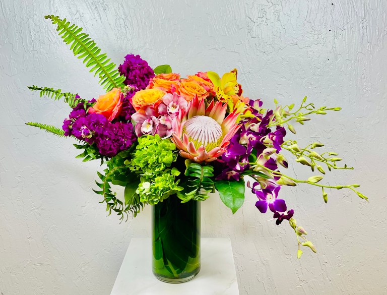 Tall cylinder vase filled with green hydrangea, pink cymbidium orchids, free spirit roses, purple stock, purple dendrobiums, green cymbidium orchids, and king protea designed by La Paloma Blanca Floral Designs in Scottsdale AZ