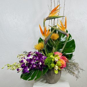 Grey Concrete Planter with Birds of Paradise, orange pincushion protea, purple dendrobium orchids, free spirit roses, green trick, and green cymbidium orchids designed by La Paloma Blanca Floral Designs in Scottsdale, AZ