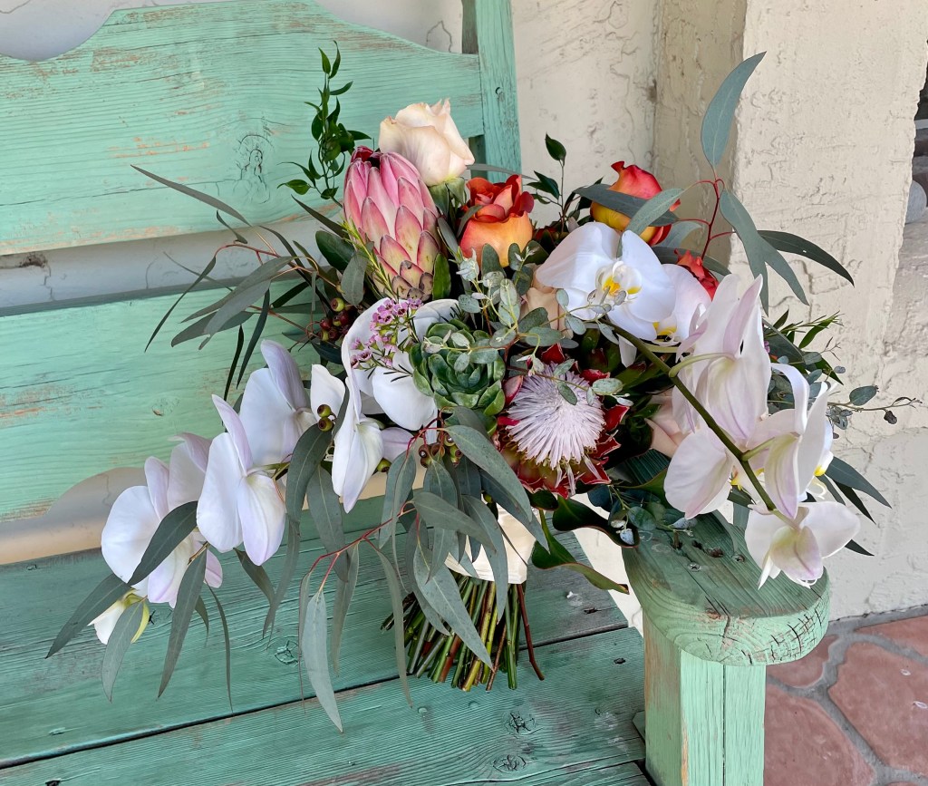 burnt orange roses, white phaelanopsis orchids, pink mink protea, champagne roses, and greens tied with a white ribbon