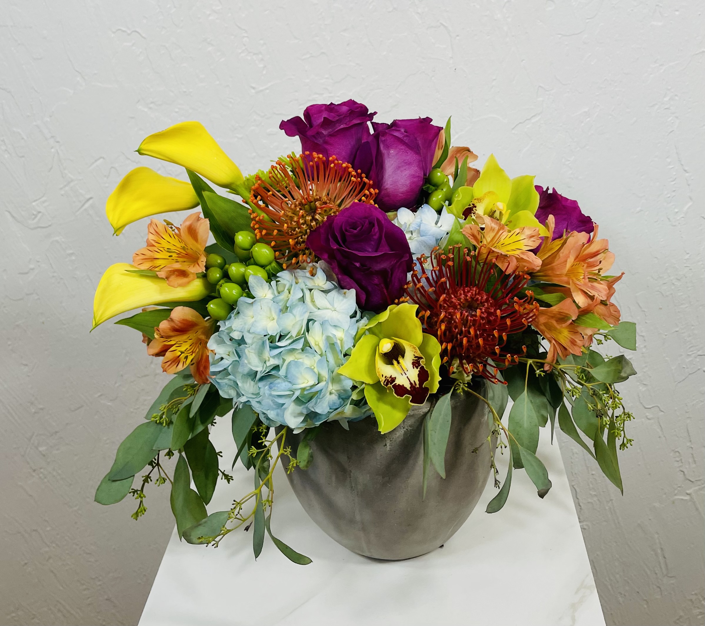 concrete planter with yellow callas, purple roses, green cymbidium orchids, pincushion protea, and hydrangea designed by La Paloma Blanca Floral Designs in Scottsdale, AZ
