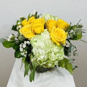 Yellow roses, green hydrangea, thistle and statice in a small hobnail jar designed by La Paloma Blanca Floral Designs