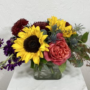 sunflower, roses, thistle, and stock in a low cube vase
