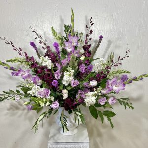white urn filled dark purple dendrobium orchids, purple gladiolus, white stock, purple liatris, and white snapdragons designed by la paloma blanca floral designs in scottsdale, az