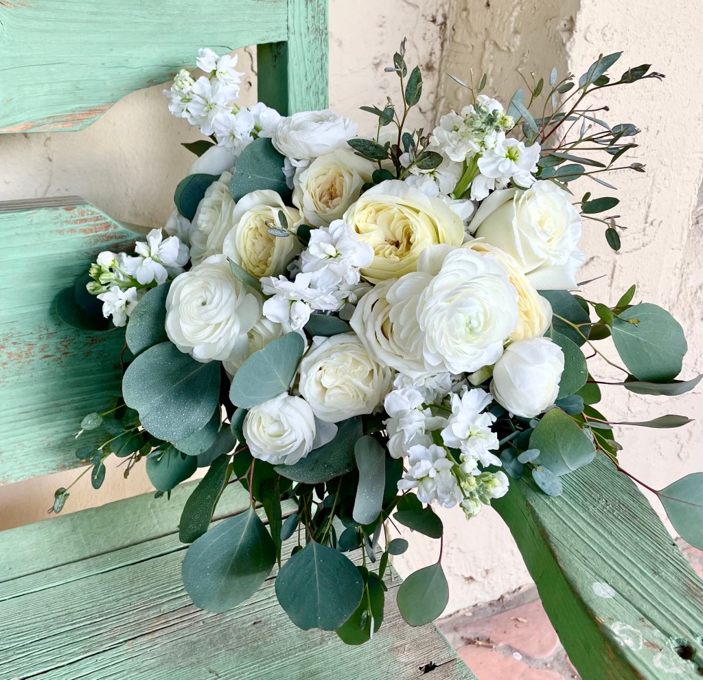 All white bridal bouquet of roses, garden roses, ranunculus, stock, and greens