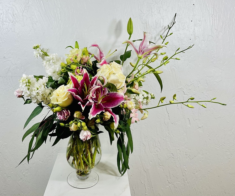 pedestal vase with stargazer lilies, roses, lisianthus, stock, and dendrobium orchids designed by la paloma blanca floral designs
