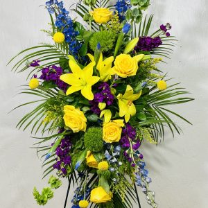 Standing Spray of yellow lilies, yellow roses, blue iris, blue delphinium, green bells of ireland, purple stock, and craspedia designed by la paloma blanca floral designs